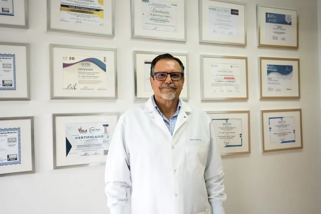 Dr. Vázquez Parnass in front of the wall of his framed certificates at the clinic